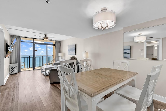 dining room with floor to ceiling windows, ceiling fan with notable chandelier, baseboards, and wood finished floors