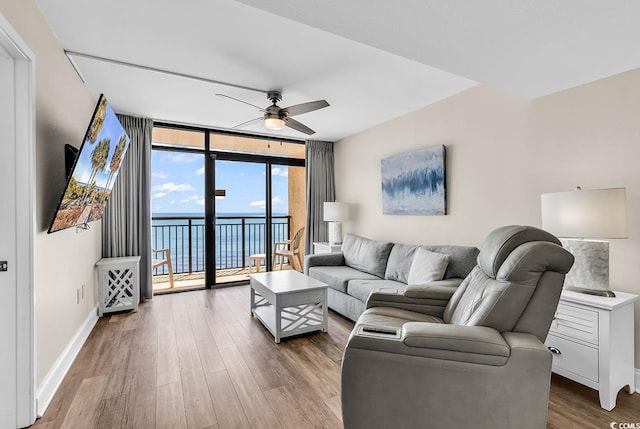 living area featuring a wall of windows, wood finished floors, ceiling fan, and baseboards