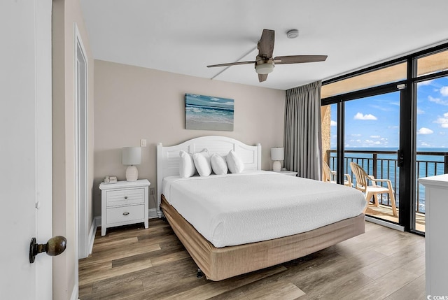 bedroom with expansive windows, access to exterior, wood finished floors, and a water view
