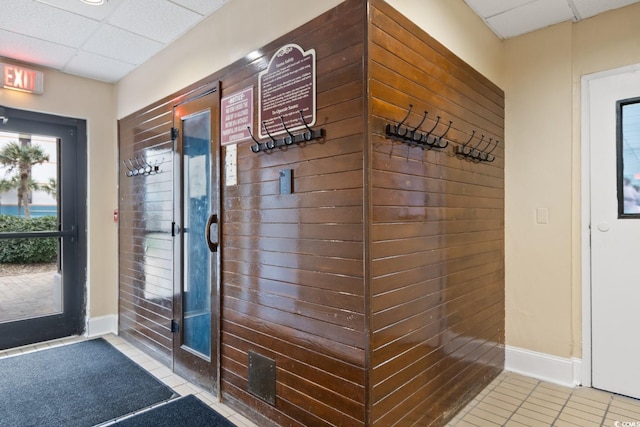 doorway with baseboards, tile patterned flooring, and a paneled ceiling