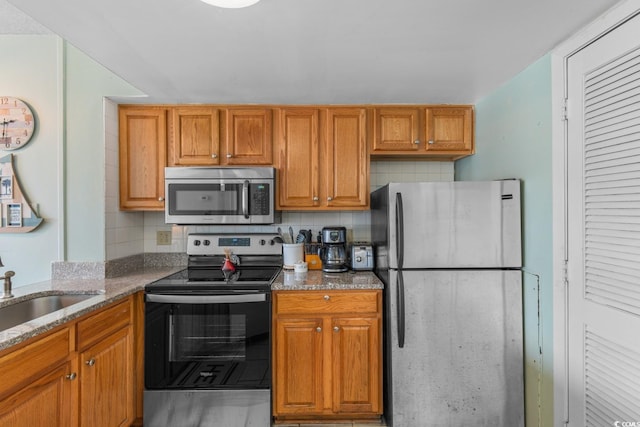 kitchen featuring stone countertops, brown cabinets, tasteful backsplash, a sink, and appliances with stainless steel finishes