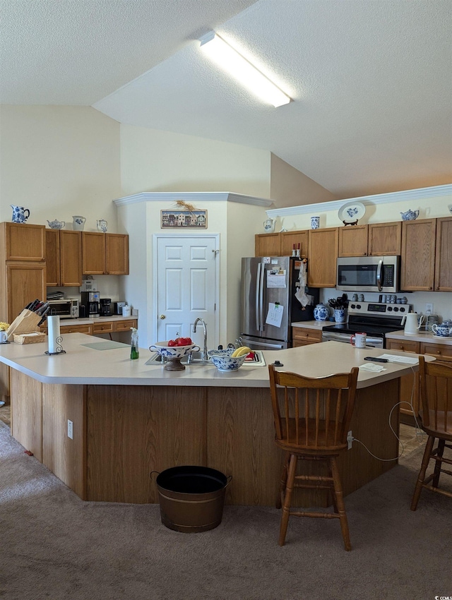 kitchen featuring appliances with stainless steel finishes, vaulted ceiling, light colored carpet, a kitchen breakfast bar, and light countertops