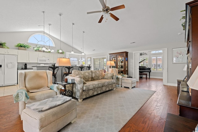 living room featuring a ceiling fan, visible vents, baseboards, high vaulted ceiling, and light wood-style floors