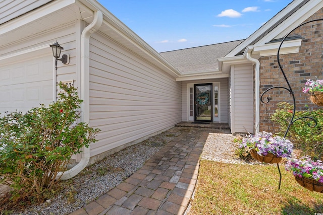 entrance to property with an attached garage and roof with shingles
