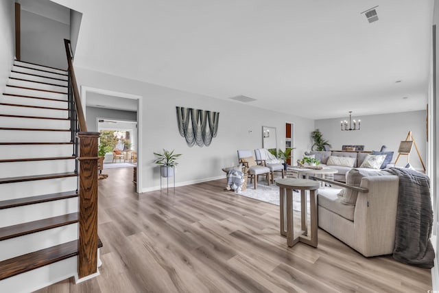 living area with visible vents, baseboards, stairway, light wood-style flooring, and a notable chandelier