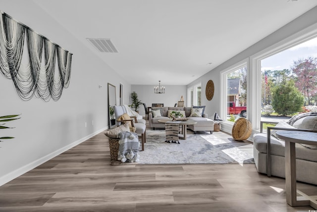 living room featuring an inviting chandelier, baseboards, wood finished floors, and visible vents