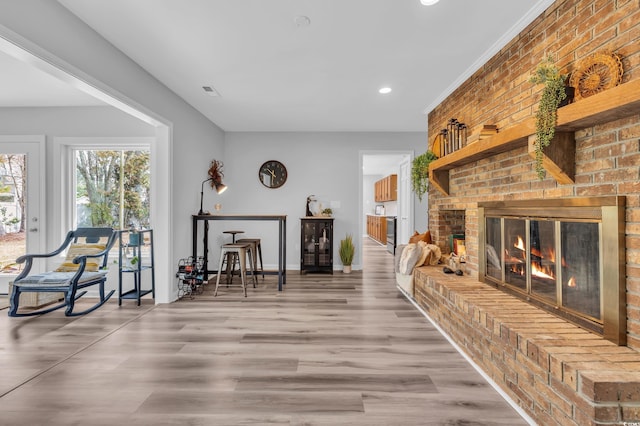 living area with visible vents, a brick fireplace, wood finished floors, baseboards, and recessed lighting