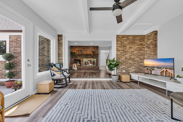 interior space with beamed ceiling, a fireplace, brick wall, and wood finished floors
