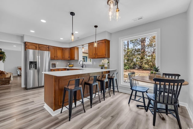 kitchen featuring stainless steel refrigerator with ice dispenser, visible vents, brown cabinets, light countertops, and a peninsula