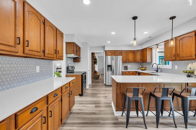 kitchen featuring a peninsula, stainless steel refrigerator with ice dispenser, electric range oven, under cabinet range hood, and a sink