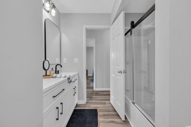 bathroom with vanity, baseboards, wood finished floors, and shower / bath combination with glass door