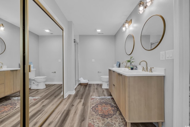 full bath with wood finished floors, toilet, two vanities, a shower stall, and a sink