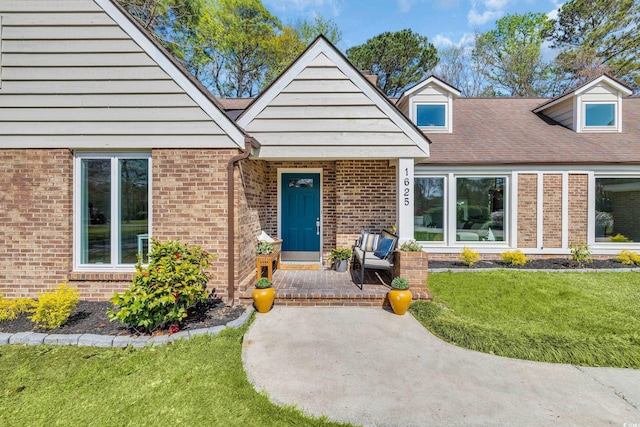 view of front of property with a shingled roof, brick siding, and a front yard