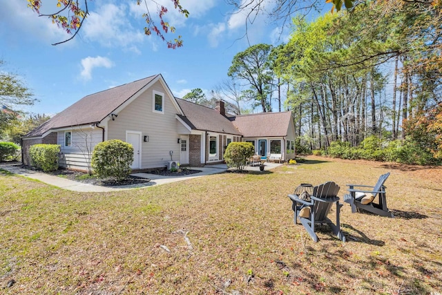 back of house with a lawn, a patio, a chimney, and a fire pit
