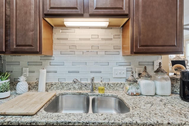 kitchen featuring backsplash, dark brown cabinets, light stone countertops, and a sink
