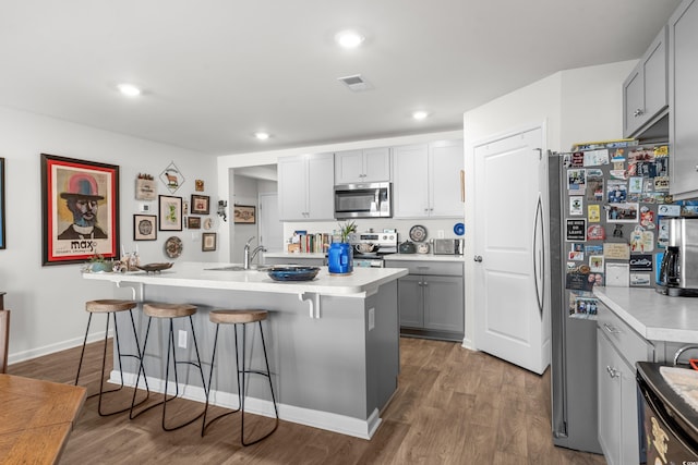 kitchen featuring light countertops, visible vents, a breakfast bar area, stainless steel appliances, and wood finished floors