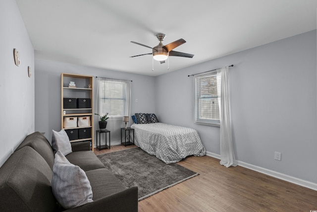 bedroom with ceiling fan, wood finished floors, baseboards, and multiple windows