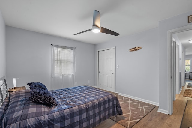 bedroom with a closet, baseboards, wood finished floors, and a ceiling fan