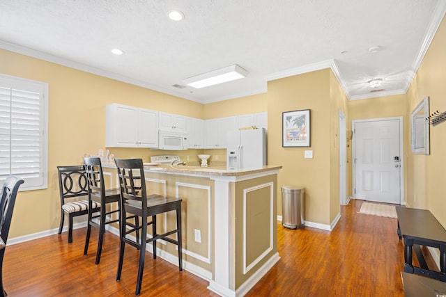 kitchen with white appliances, a peninsula, a breakfast bar, and dark wood-type flooring