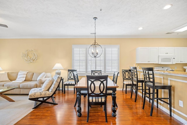dining area with ornamental molding, dark wood finished floors, a textured ceiling, and a chandelier