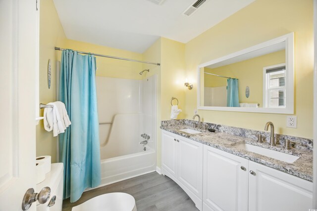 full bathroom with wood finished floors, visible vents, shower / tub combo with curtain, and a sink