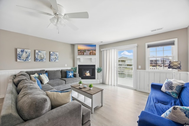 living area featuring wainscoting, a ceiling fan, visible vents, and light wood finished floors