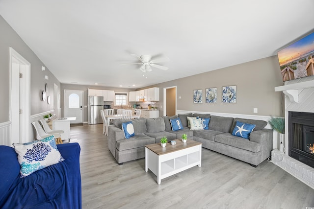 living area featuring light wood-style flooring, wainscoting, recessed lighting, a ceiling fan, and a brick fireplace