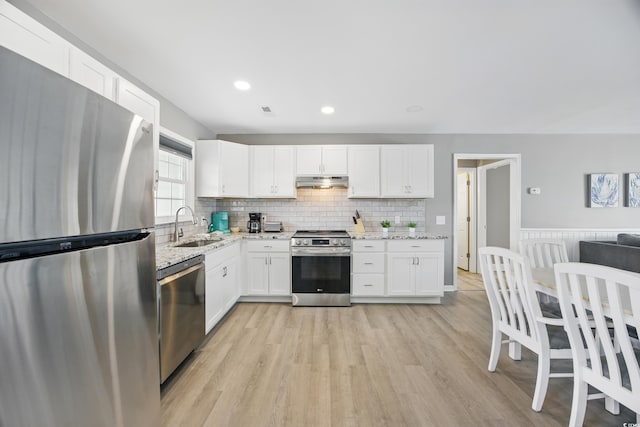 kitchen featuring stainless steel appliances, a sink, backsplash, light stone countertops, and under cabinet range hood