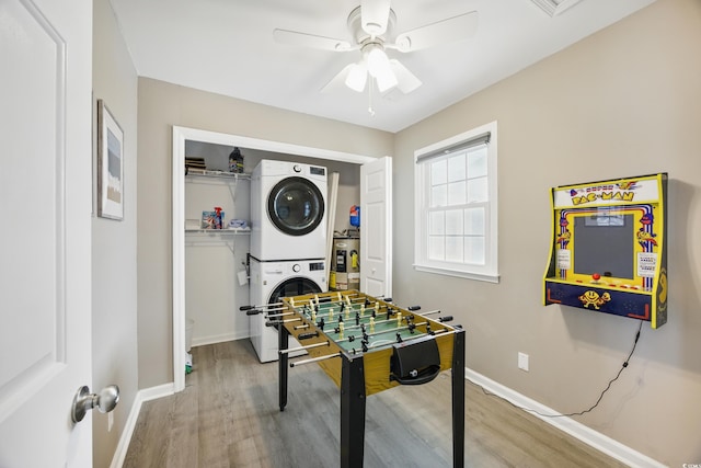 game room featuring baseboards, a ceiling fan, stacked washer / dryer, and wood finished floors