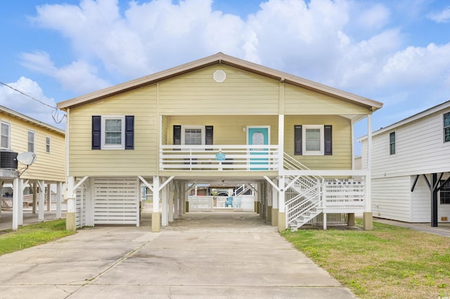 coastal inspired home featuring a carport, covered porch, stairs, and concrete driveway