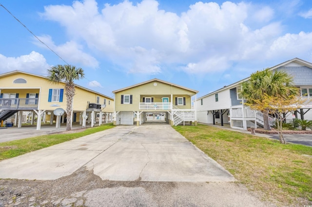 raised beach house featuring stairway, driveway, a front yard, and a carport