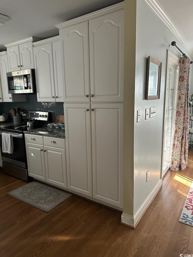 kitchen featuring dark countertops, baseboards, white cabinetry, dark wood-type flooring, and appliances with stainless steel finishes