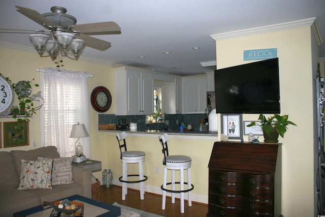 kitchen with a ceiling fan, a breakfast bar, backsplash, a peninsula, and ornamental molding