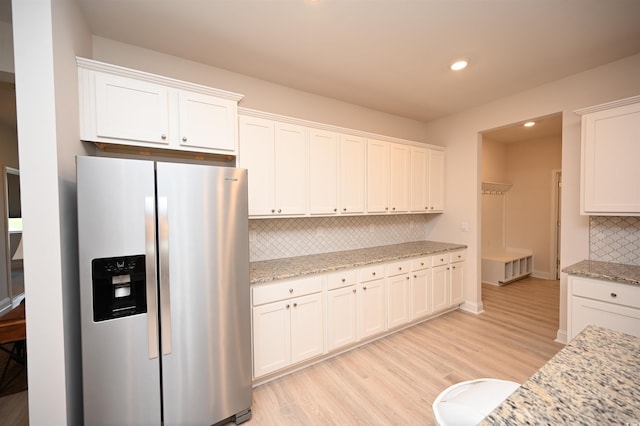 kitchen with light stone countertops, light wood-style floors, stainless steel refrigerator with ice dispenser, white cabinets, and backsplash