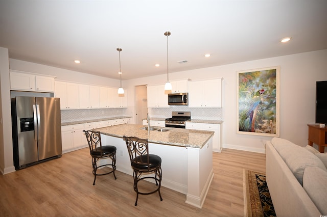 kitchen with stainless steel appliances, a sink, light wood finished floors, and tasteful backsplash
