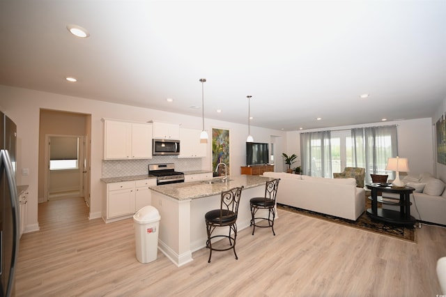 kitchen with appliances with stainless steel finishes, a sink, a kitchen breakfast bar, open floor plan, and backsplash