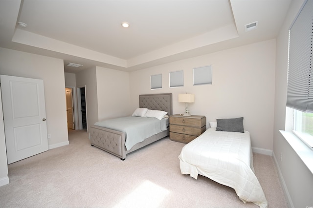 bedroom with a tray ceiling, visible vents, light carpet, and baseboards