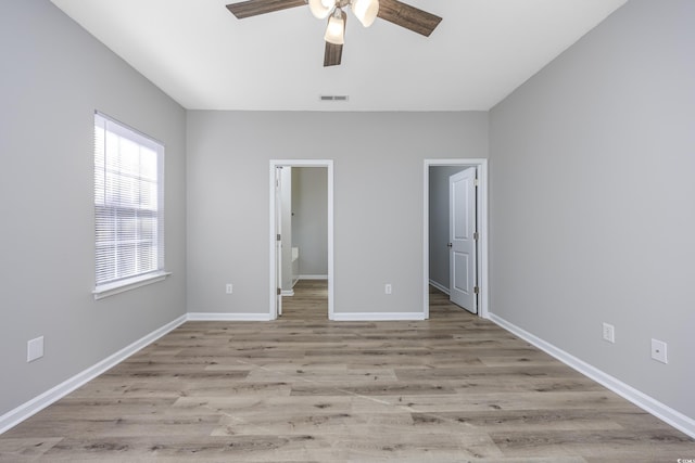 unfurnished bedroom with wood finished floors, visible vents, ceiling fan, a walk in closet, and baseboards