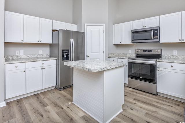 kitchen with light wood-style floors, white cabinets, appliances with stainless steel finishes, and a towering ceiling