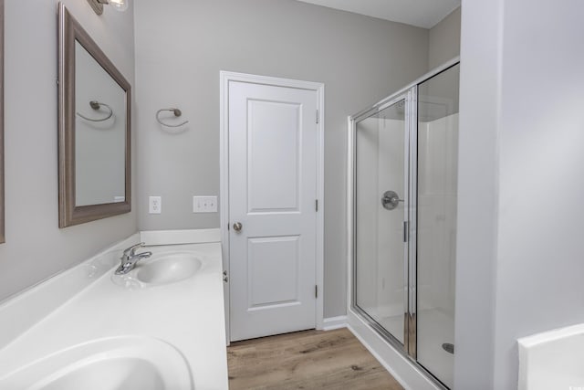 full bathroom featuring a shower stall, double vanity, a sink, and wood finished floors