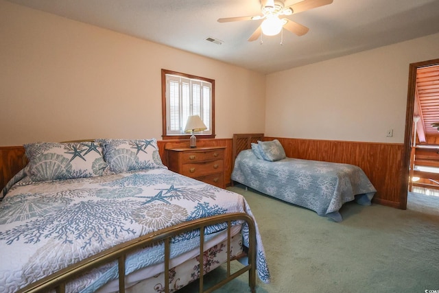 bedroom with carpet flooring, wooden walls, a wainscoted wall, visible vents, and ceiling fan