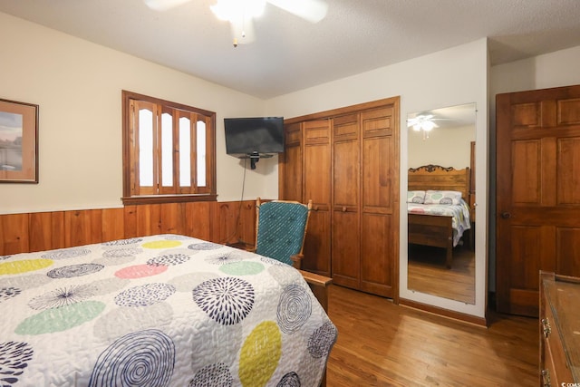 bedroom with a closet, ceiling fan, wooden walls, wainscoting, and wood finished floors