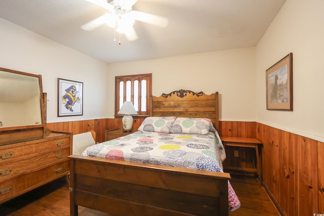 bedroom with wood walls, ceiling fan, wainscoting, and dark wood finished floors