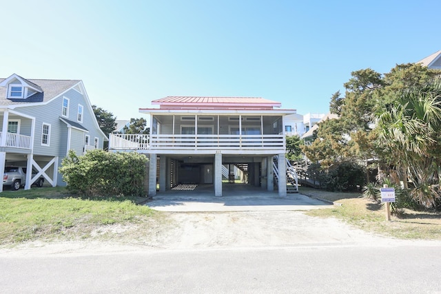 beach home featuring driveway, a sunroom, a carport, metal roof, and a standing seam roof