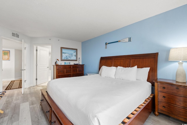 bedroom with baseboards, light wood finished floors, and visible vents