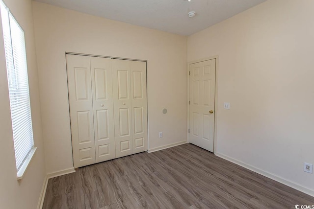 unfurnished bedroom featuring baseboards, wood finished floors, and a closet