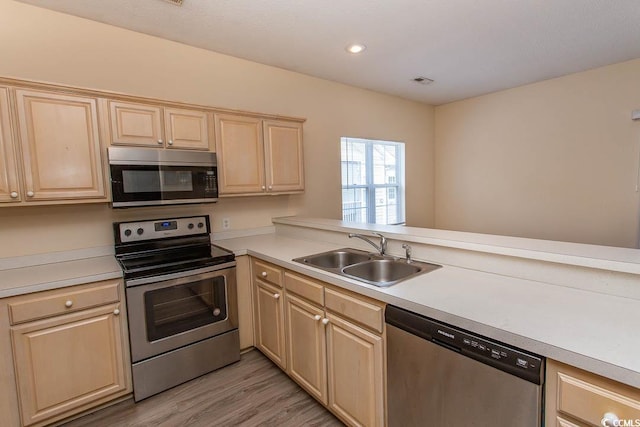 kitchen with light brown cabinetry, a sink, light countertops, light wood-style flooring, and stainless steel appliances