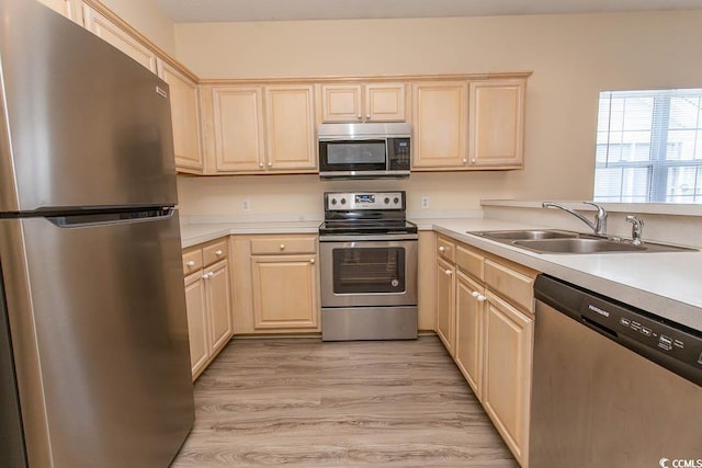 kitchen with light brown cabinets, light countertops, a sink, light wood-style flooring, and stainless steel appliances