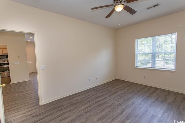 unfurnished room with visible vents, dark wood finished floors, ceiling fan, and baseboards
