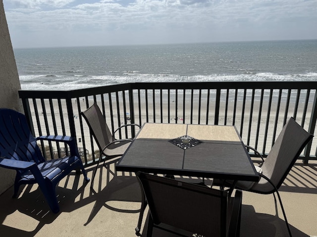 balcony featuring a water view, outdoor dining area, and a view of the beach
